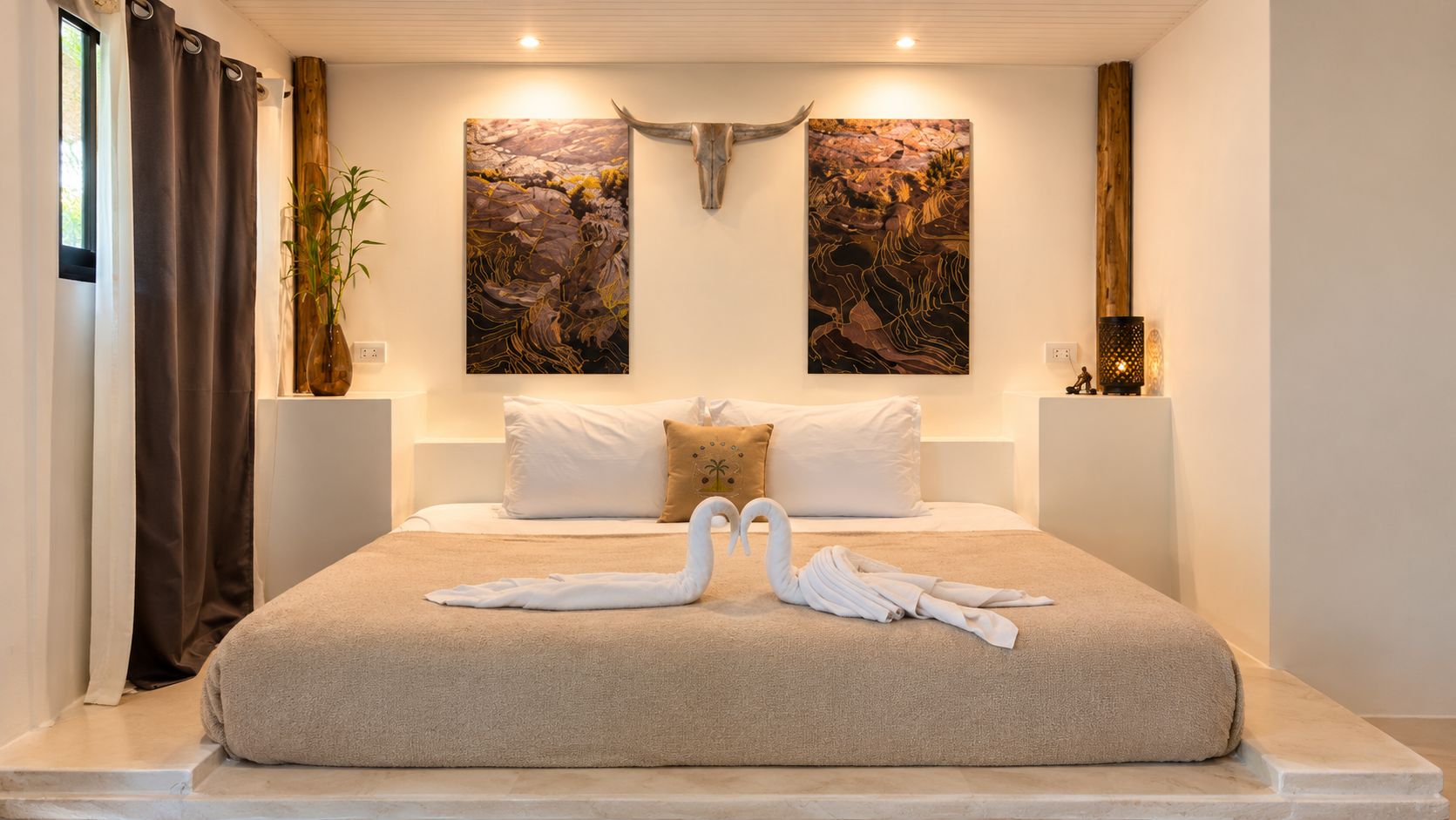 Habitación de hotel con una cama grande, dos obras de arte colgadas en la pared, un cabecero de madera y una decoración de toallas con forma de cisne.