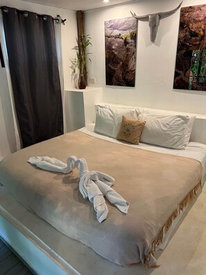 A neatly made bed with a towel and a decorative swan, a potted plant, and two wall art pieces.