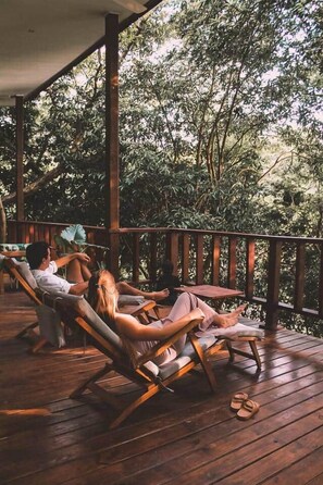 A wooden deck with lounge chairs, surrounded by dense foliage.