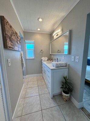 A bathroom with a white vanity, a large mirror, and a potted plant. - The Cape Escape | Cape Coral (Cape Coral)