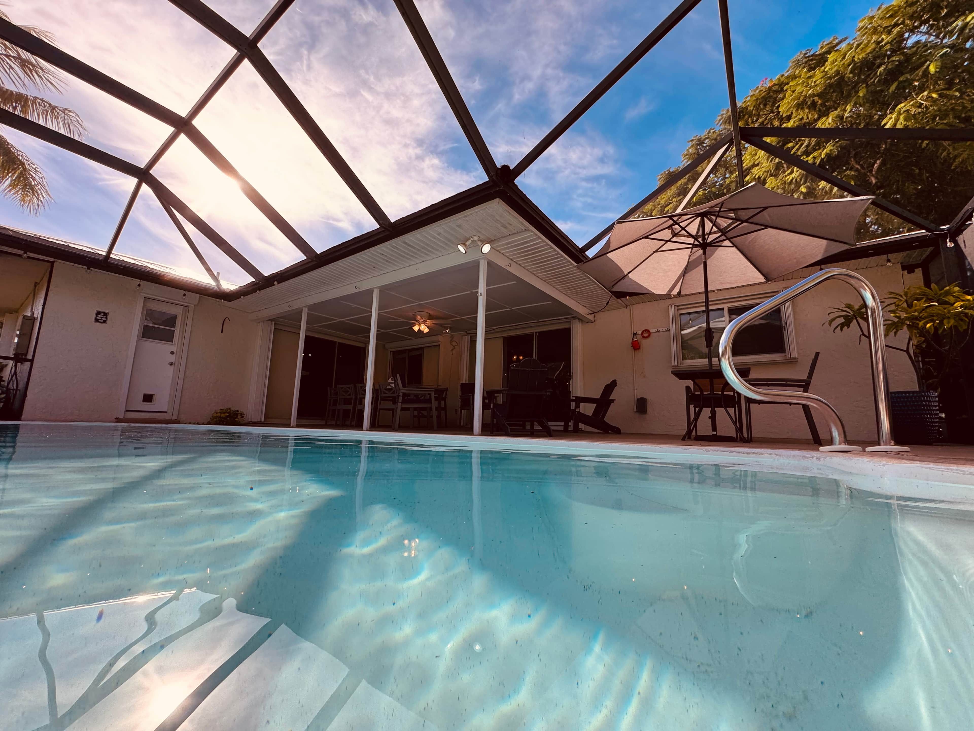 An indoor swimming pool with clear water, surrounded by a covered patio area with chairs and a table.