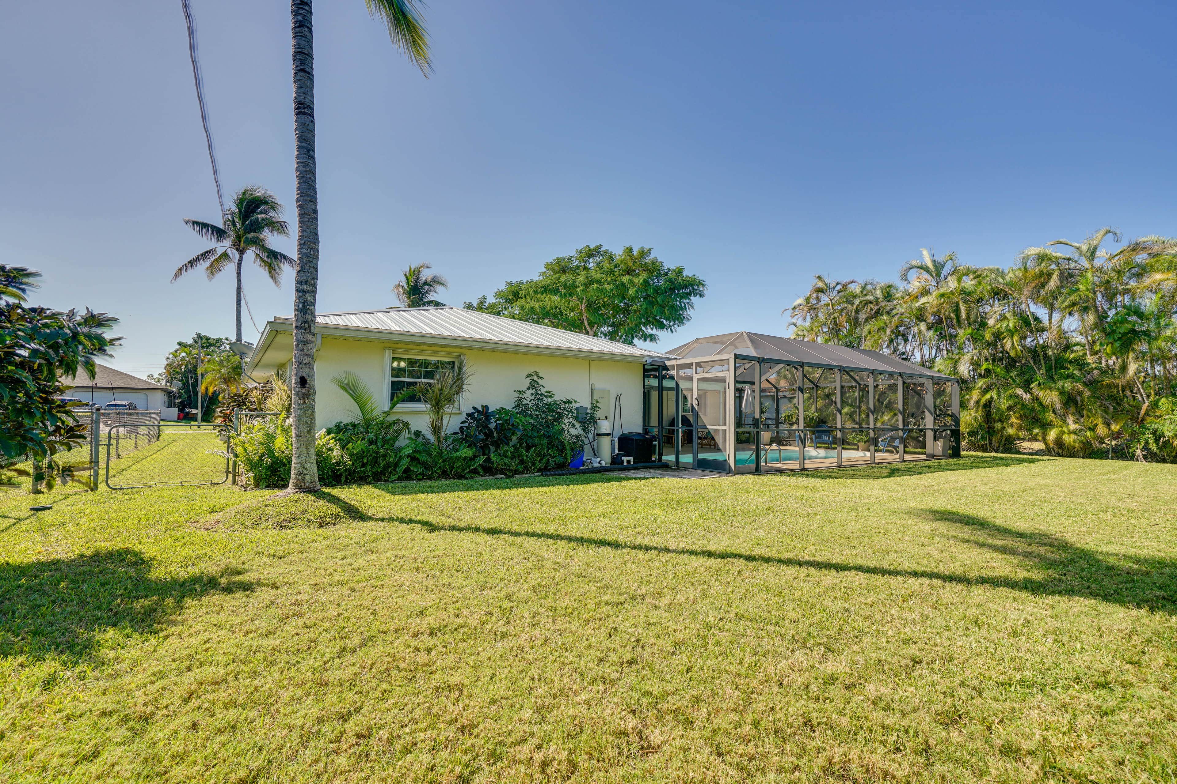 Una casa de un piso con patio cercado, piscina y palmeras.