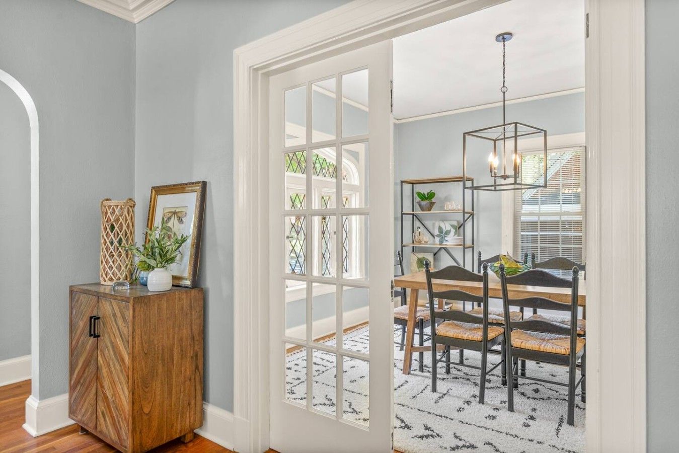 A room with a wooden cabinet, a dining table with chairs, and a view through a glass door.