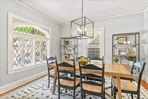 Ein Esszimmer mit Holztisch, schwarzen Stühlen, einem geometrischen Kronleuchter und einem gemusterten Teppich.