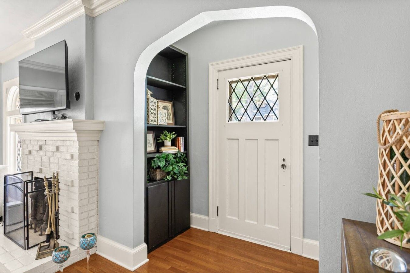 A hallway with a white door, a black bookshelf, a white fireplace, and a television mounted above it.
