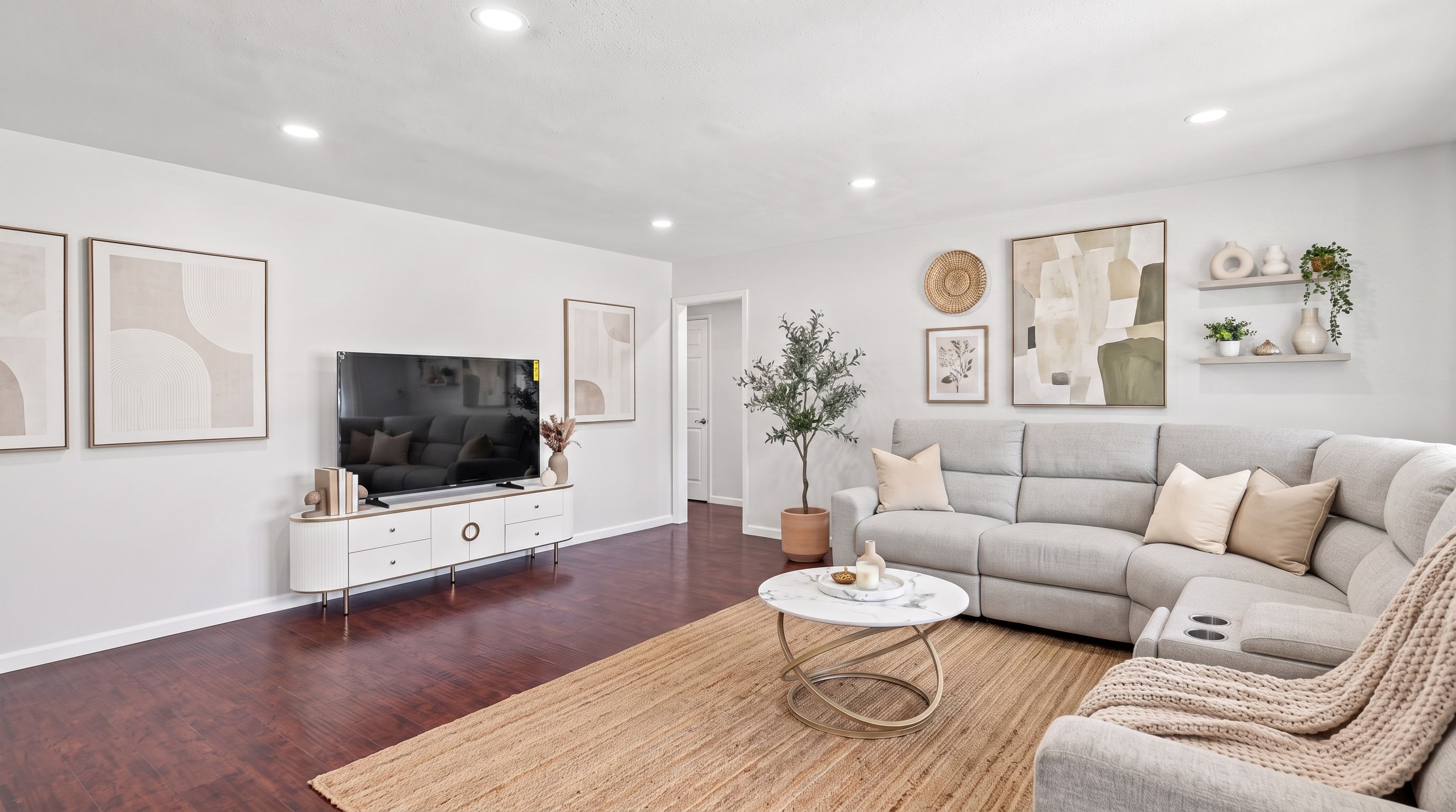 A modern living room with a flat-screen TV, a grey sofa, a coffee table, and a potted plant.
