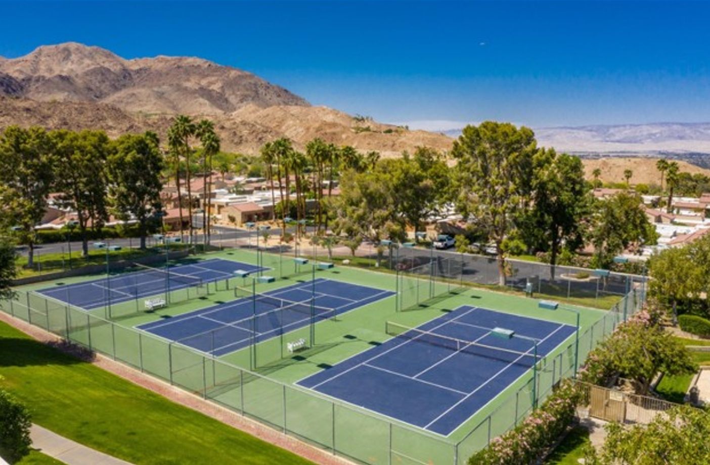 Complejo de canchas de tenis con varias canchas, rodeado de zonas verdes y edificios residenciales.