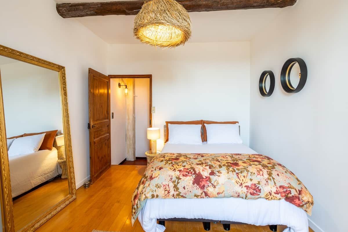 Une chambre avec un grand lit, un miroir, une porte et un luminaire suspendu.
