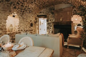 A rustic interior with stone walls, a fireplace, a dining table set for two, and wicker furniture. - L’Oustau des Martinets (Aureille)