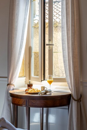 A window with curtains, a table with a glass of orange juice, a plate of croissants, and a jar of jam. - L’Oustau des Martinets (Aureille)
