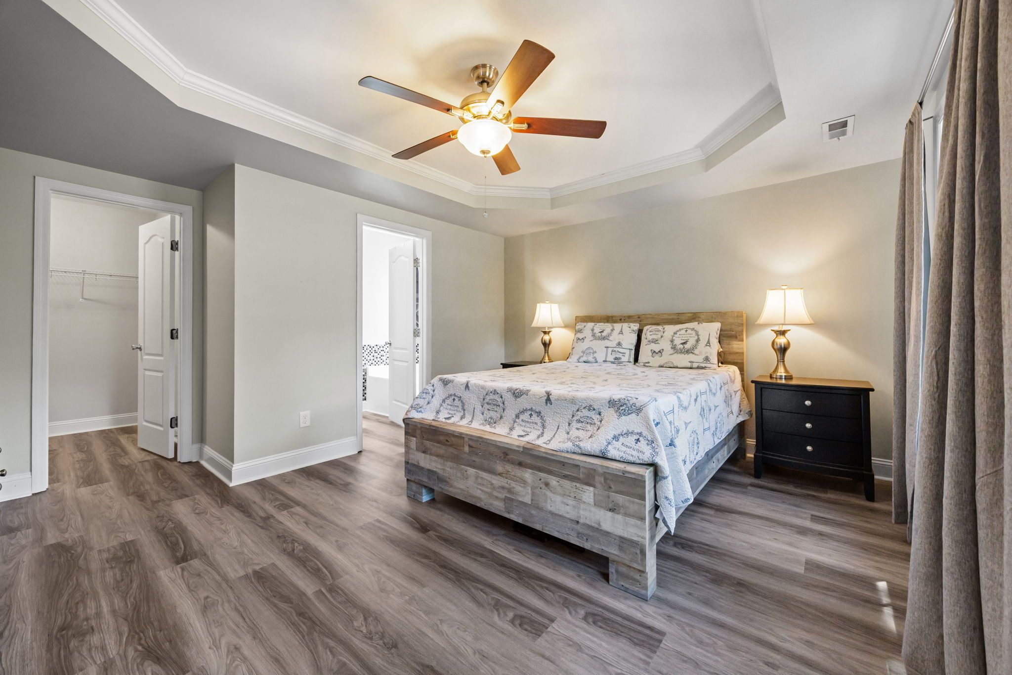 A bedroom with a bed, bedside tables, a ceiling fan, and a door.