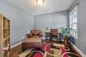 Una habitación con un sofá de cuero marrón, una silla de madera, una mesita con una planta y un ventanal grande.