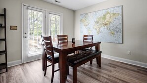 Une salle à manger avec une table en bois, quatre chaises, un banc, une grande carte du monde accrochée au mur et une porte-fenêtre coulissante.