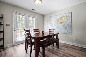 A dining room with a wooden table, four chairs, a bench, a large world map on the wall, and a sliding glass door. - Colonial Hills Hideaway - 2 Bedroom Home with Spacious Yard (Lillington)