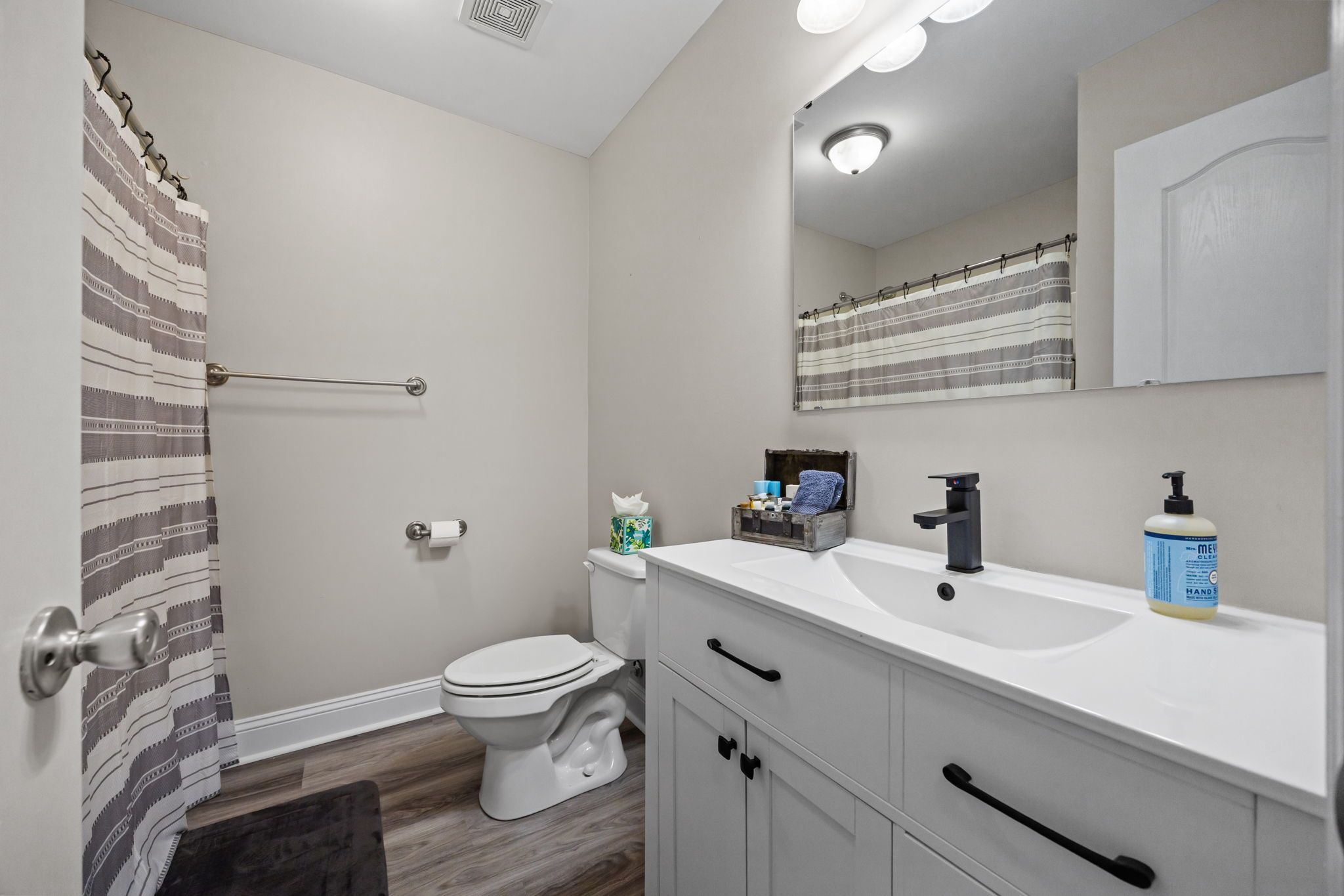 A bathroom with a toilet, sink, mirror, and shower curtain.