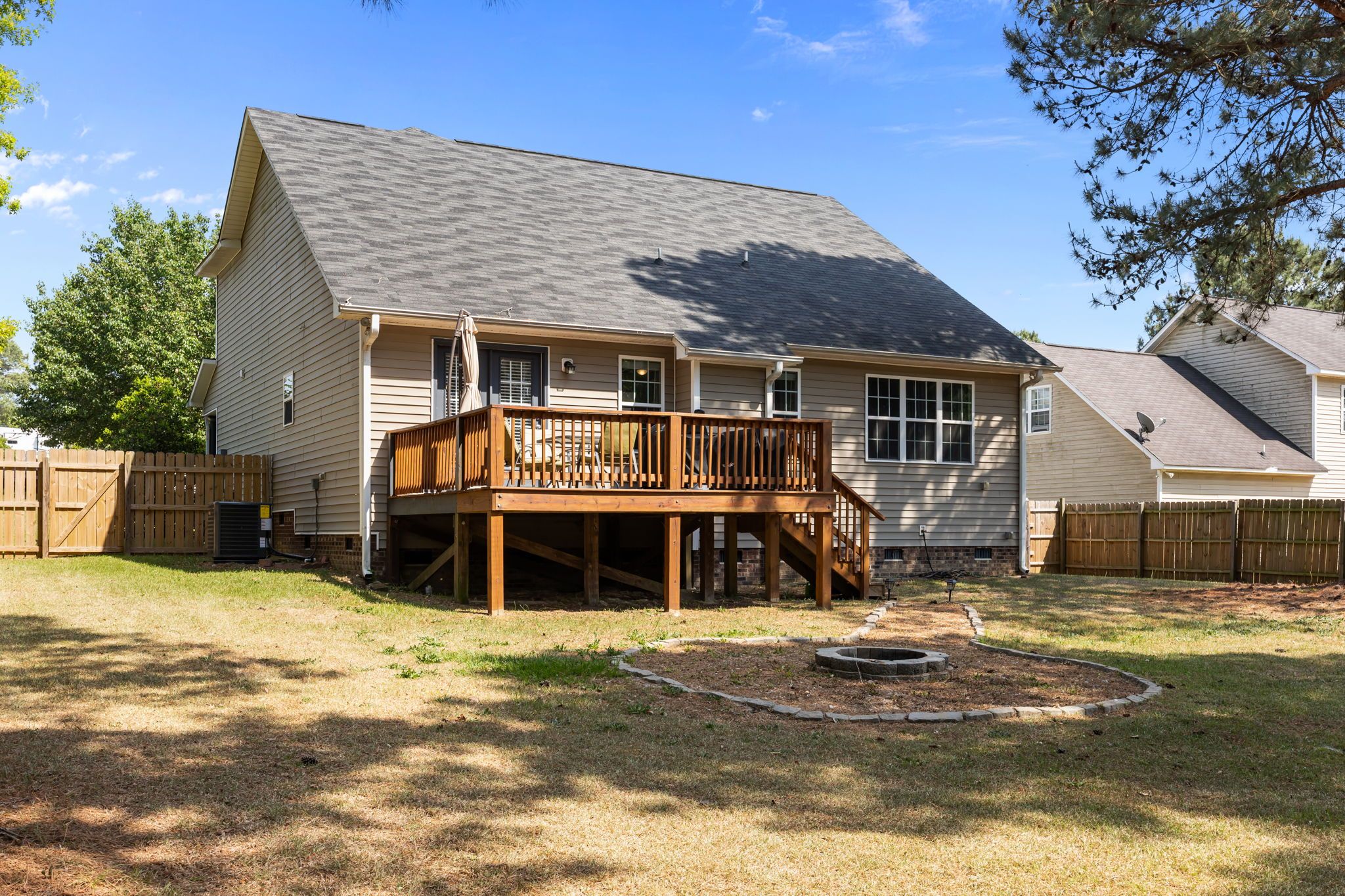 A two-story house with a wooden deck, a fenced yard, and a fire pit.