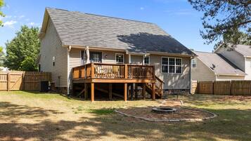 A two-story house with a wooden deck, a fenced yard, and a fire pit.