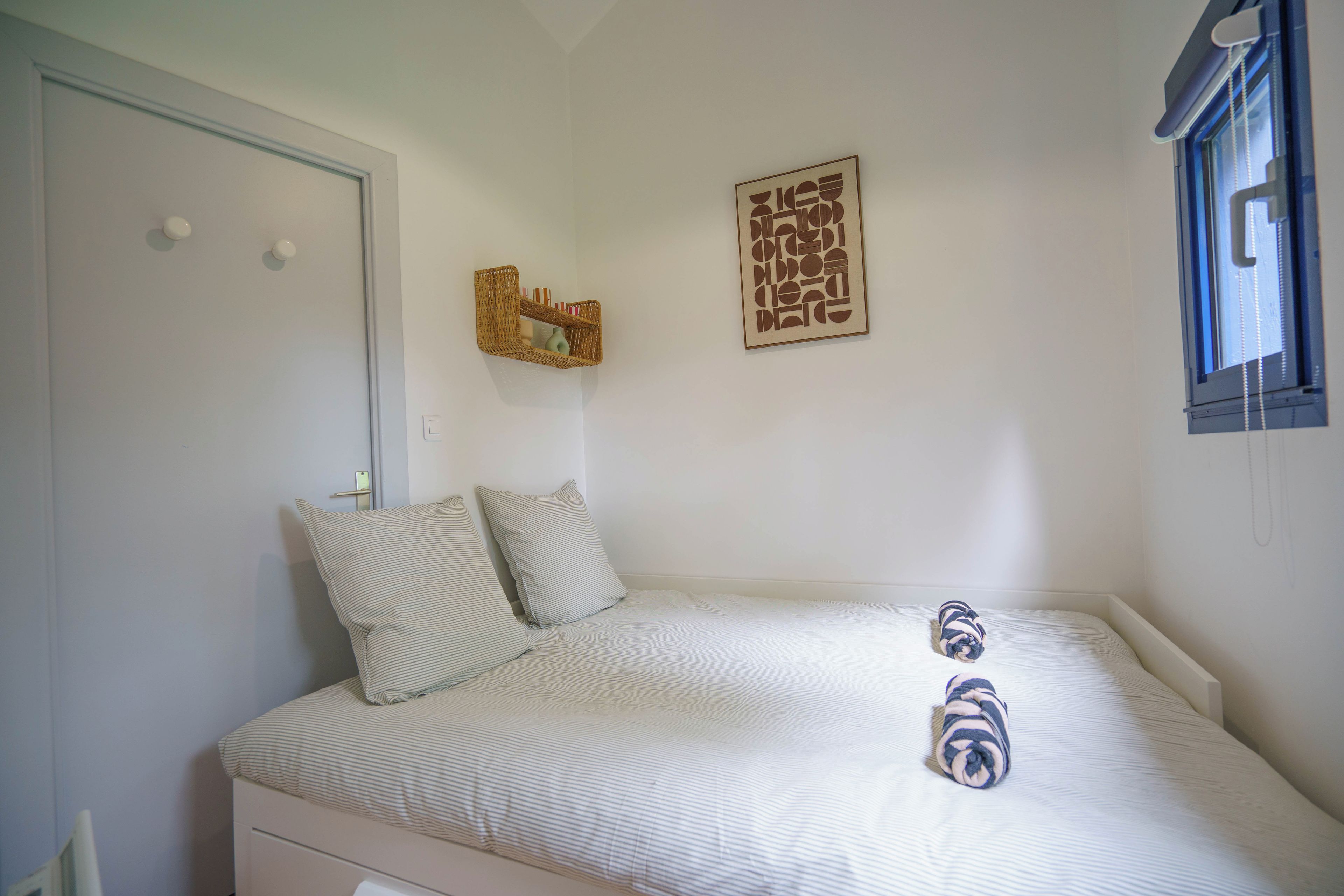 Ein Schlafzimmer mit einem Bett, Kissen, einem an der Wand befestigten Regal und einem Fenster.