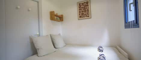A bedroom with a bed, pillows, a wall-mounted shelf, and a window.