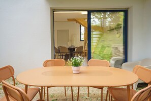 A round table with six chairs, a potted plant, and a view of an indoor dining area through a glass door. - La Vague Douce - Mer & Pinède, plage accès à pied (Douarnenez)