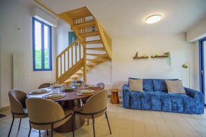 A dining area with a wooden staircase, a blue sofa, and a small table with chairs. - La Vague Douce - Mer & Pinède, plage accès à pied (Douarnenez)