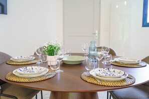 A round dining table set with plates, glasses, and a vase of flowers. - La Vague Douce - Mer & Pinède, plage accès à pied (Douarnenez)