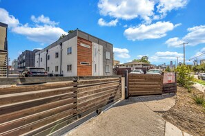 A modern building with a mix of white and wooden paneling, a gated entrance, and a clear sky. - Comfy 1BR l Sleeps 4 l Near DT w/ Free Parking (Dallas)