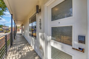 A covered outdoor corridor with a number '205' on the wall, a door with a keypad lock, and a window with a view of the street. - Comfy 1BR l Sleeps 4 l Near DT w/ Free Parking (Dallas)