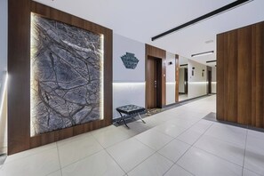 A modern hotel lobby with a large abstract wall art, a reception desk, and a wooden panel wall. - Warsaw Green Żoliborz Apt — Parking & Balcony (Warszawa)