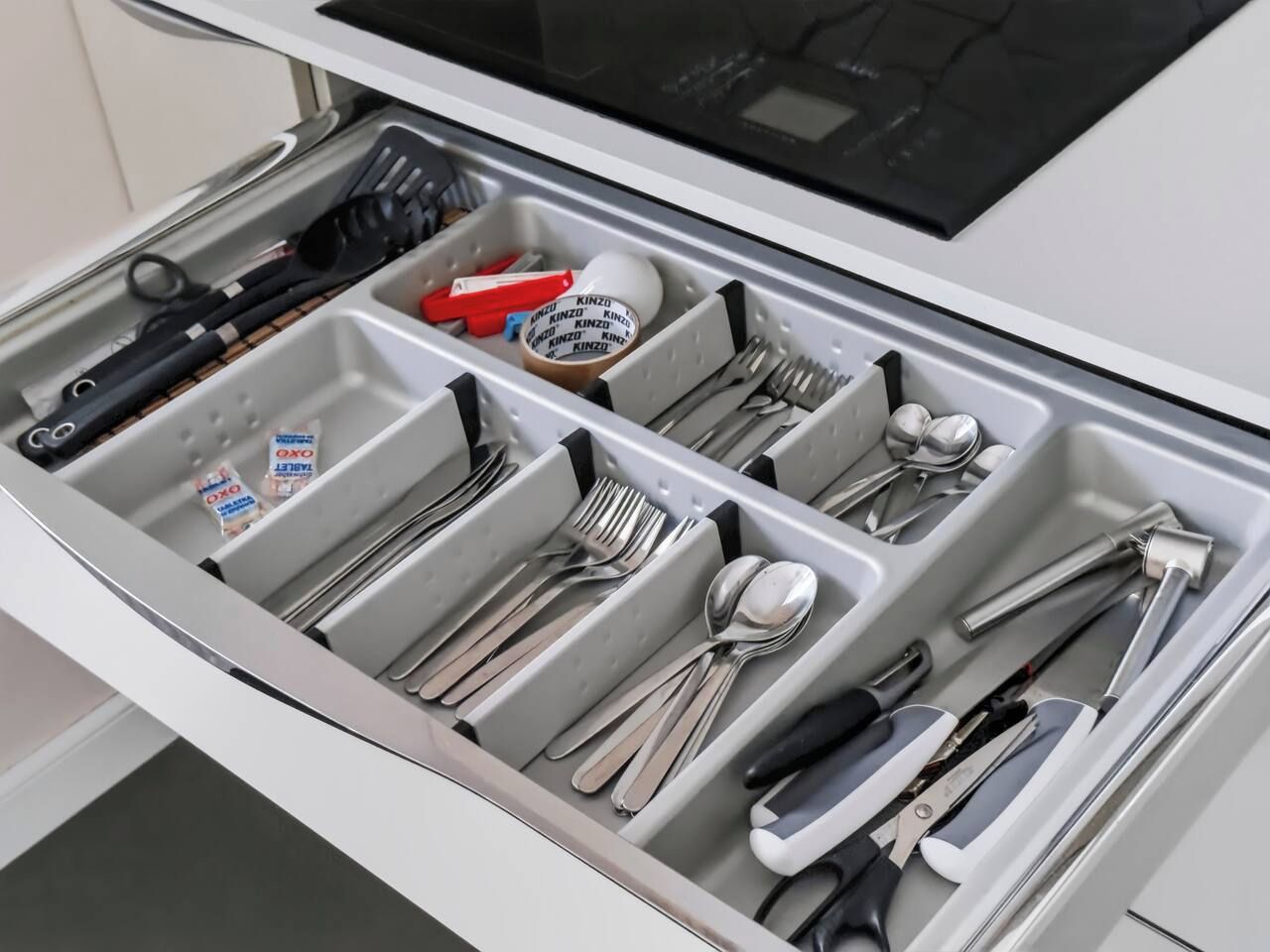 A drawer with utensils and kitchen tools organized in compartments.