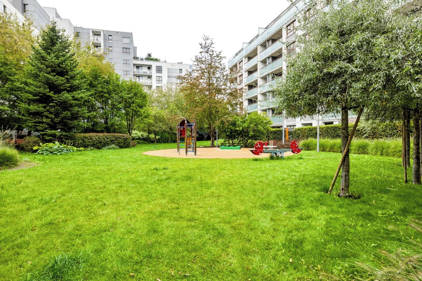 Ett bostadsområde med en lekplats, träd och hyreshus.