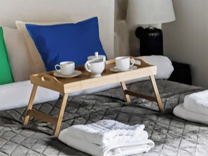 Ein Bett mit Tablett, auf dem eine Tasse und ein Teekessel stehen, ein Kissen und eine Lampe im Hintergrund.