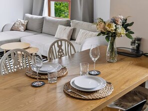 A dining table set with plates, glasses, and cutlery, with a sofa and a vase of flowers in the background. - Warsaw Green Żoliborz Apt — Parking & Balcony (Warszawa)