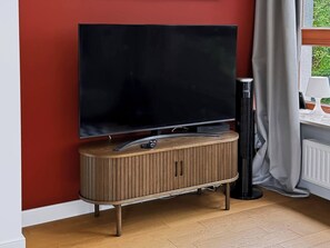 Ein Flachbildfernseher an einer Holzwandbefestigung, daneben ein schwarzer Standfuß.