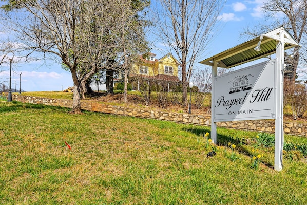 A sign for Prospect Hill with a stone wall and a house in the background.