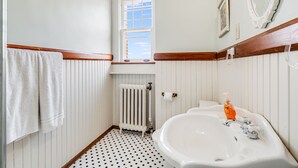 Ein Badezimmer mit einem weißen Waschbecken, einem Fenster, einer Heizung und einem Handtuchhalter.