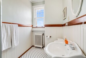 Une salle de bain avec un lavabo blanc, une fenêtre, un radiateur et un porte-serviettes.