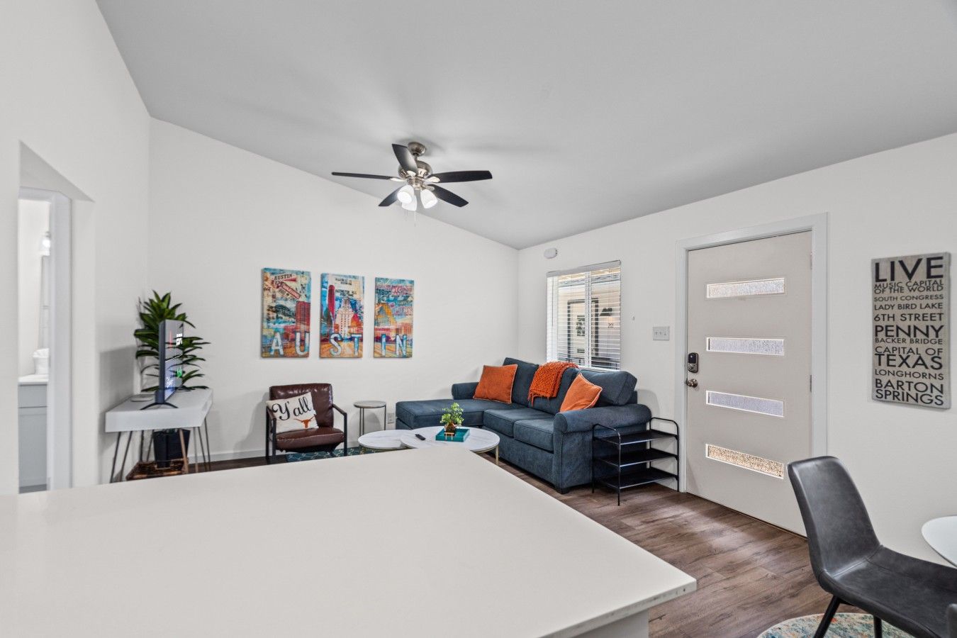 A modern living room with a dining area, a ceiling fan, and a door with a sign.