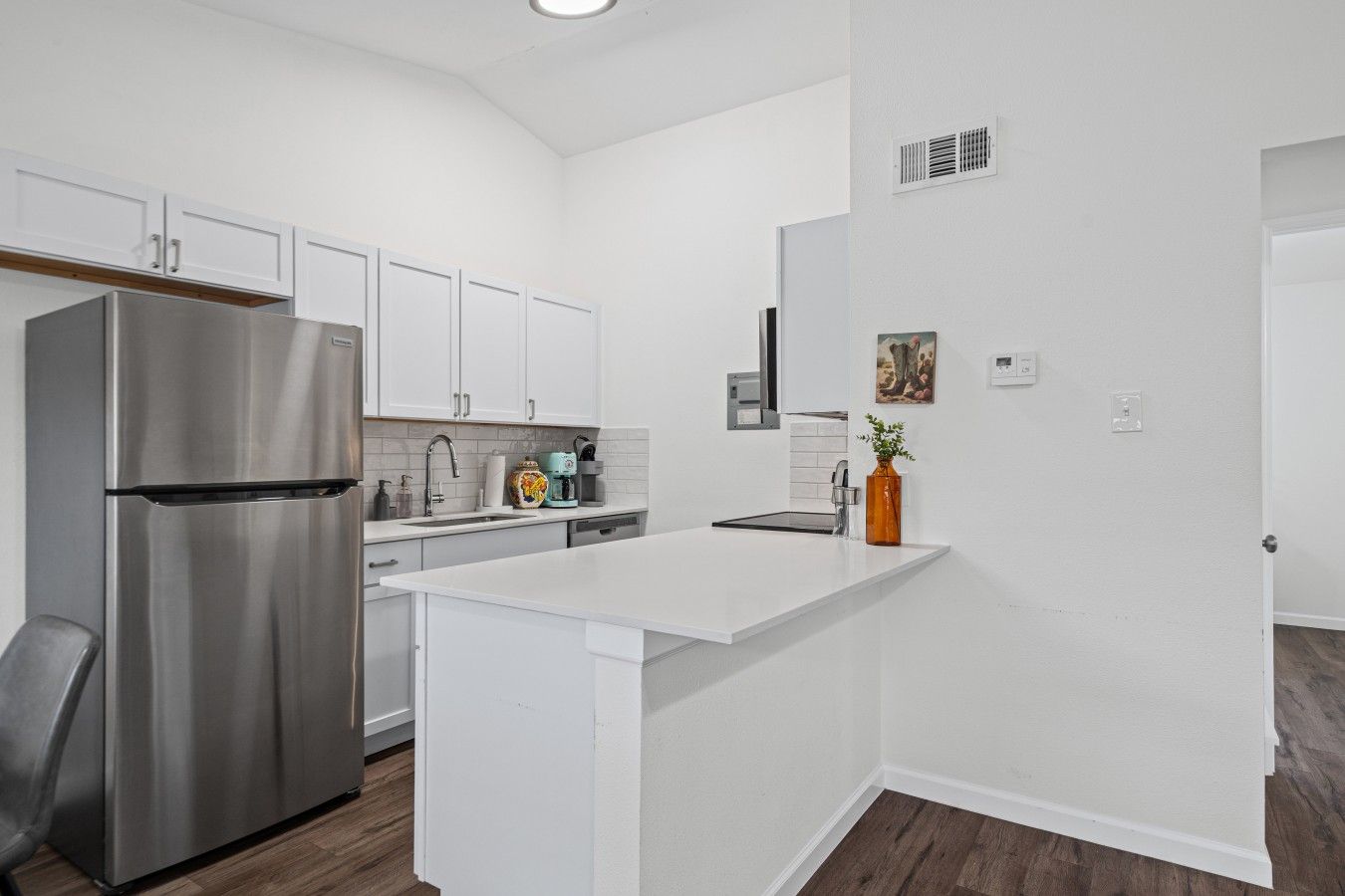 A modern kitchen with white cabinetry, a stainless steel refrigerator, a built-in oven, and a small island with a sink.