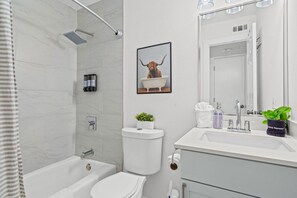 A modern bathroom with a bathtub, toilet, and sink area. - Cozy North Campus Condo w/ WFH Desk Nook, Free Parking & In-Unit Laundry (Austin)