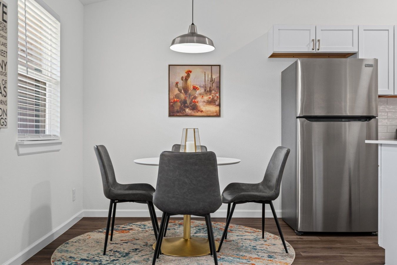A modern kitchen with a stainless steel refrigerator, a round dining table with two chairs, and a pendant light.