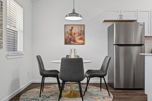 Una cocina moderna con un refrigerador de acero inoxidable, una mesa redonda para dos personas y una lámpara colgante.