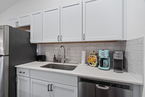 Una cocina moderna con gabinetes blancos, un refrigerador de acero inoxidable, un lavamanos, un tostador, una cafetera y un lavavajillas.