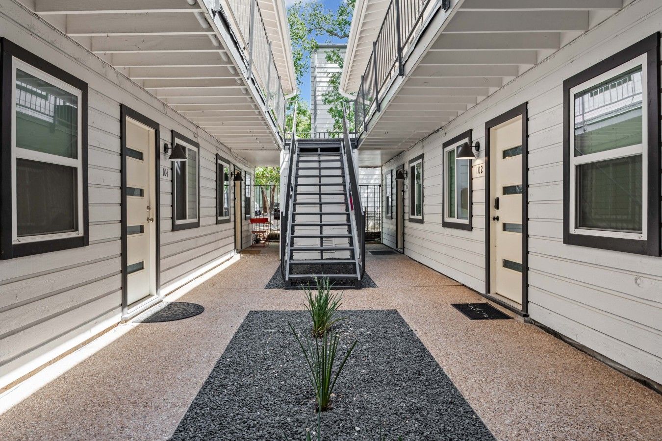 A corridor with a central staircase leading to an upper level, flanked by doors and windows.