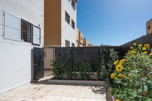 A courtyard with a tiled floor, a black gate, and a building with multiple windows.
