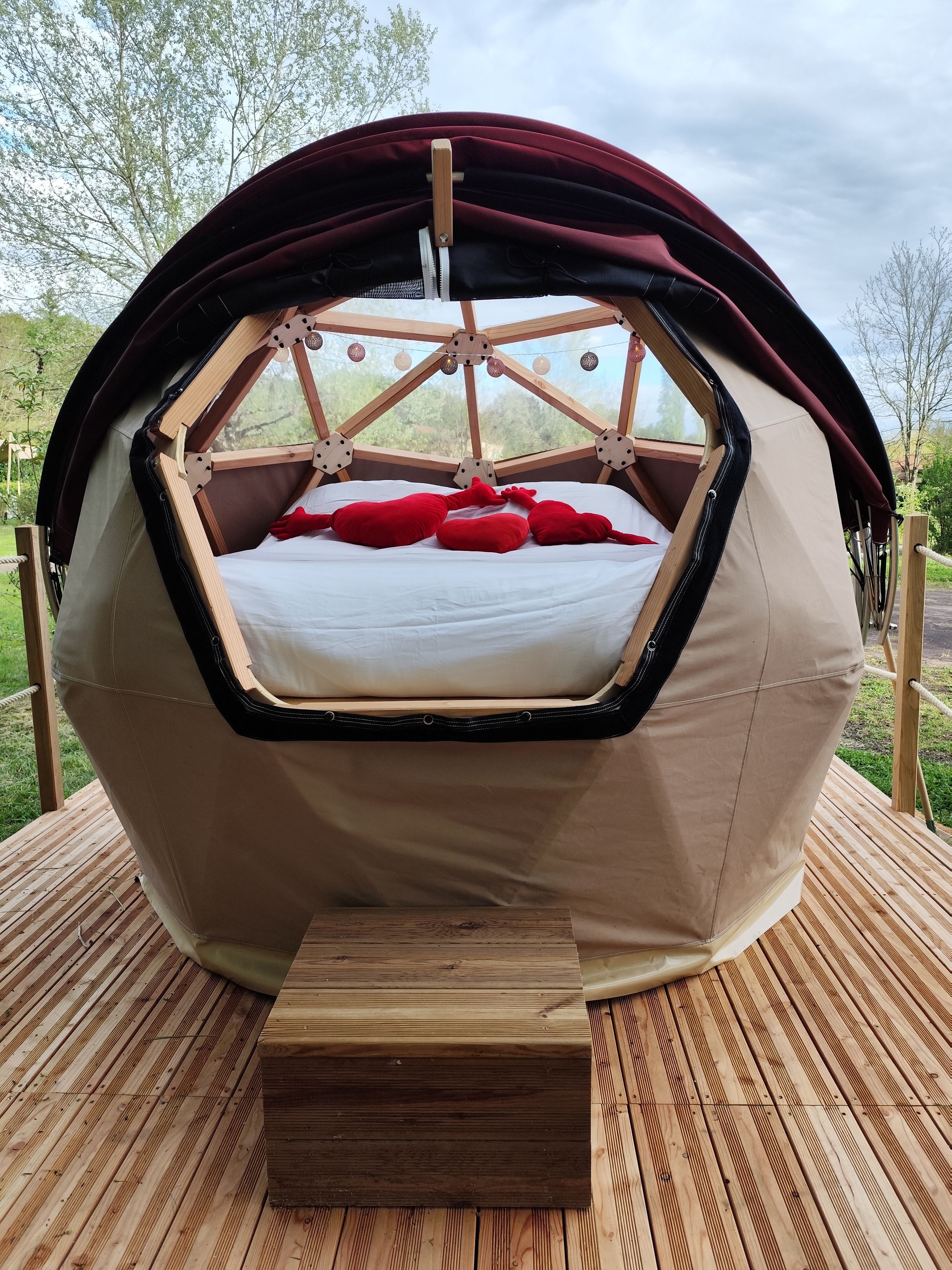 A hexagonal tent with a bed inside, featuring a wooden frame and a red canopy.