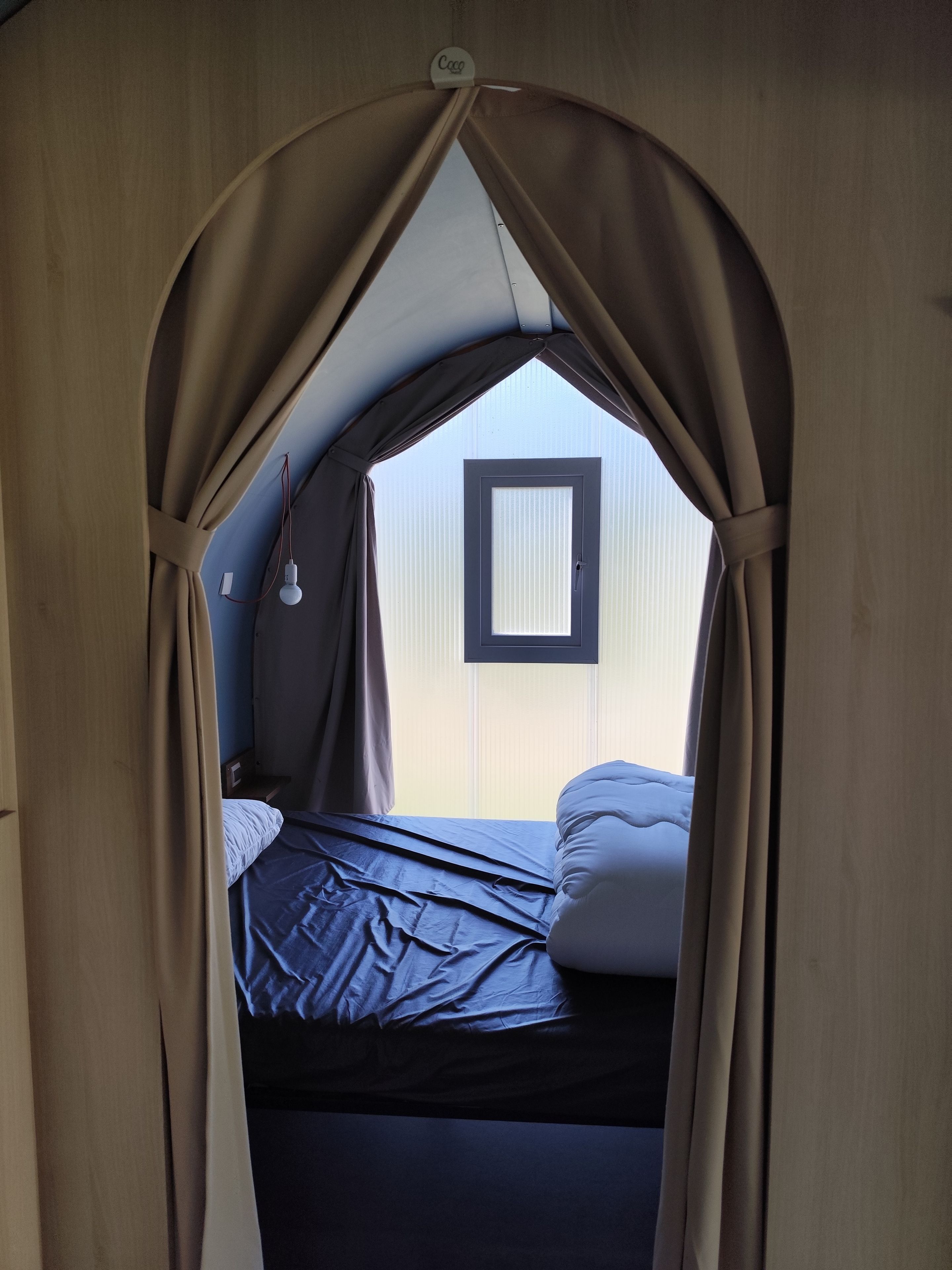 Une pièce en forme de tente, avec un lit, une lampe suspendue et une fenêtre.