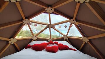 A room with a sloped ceiling, wooden beams, and a bed with red pillows.