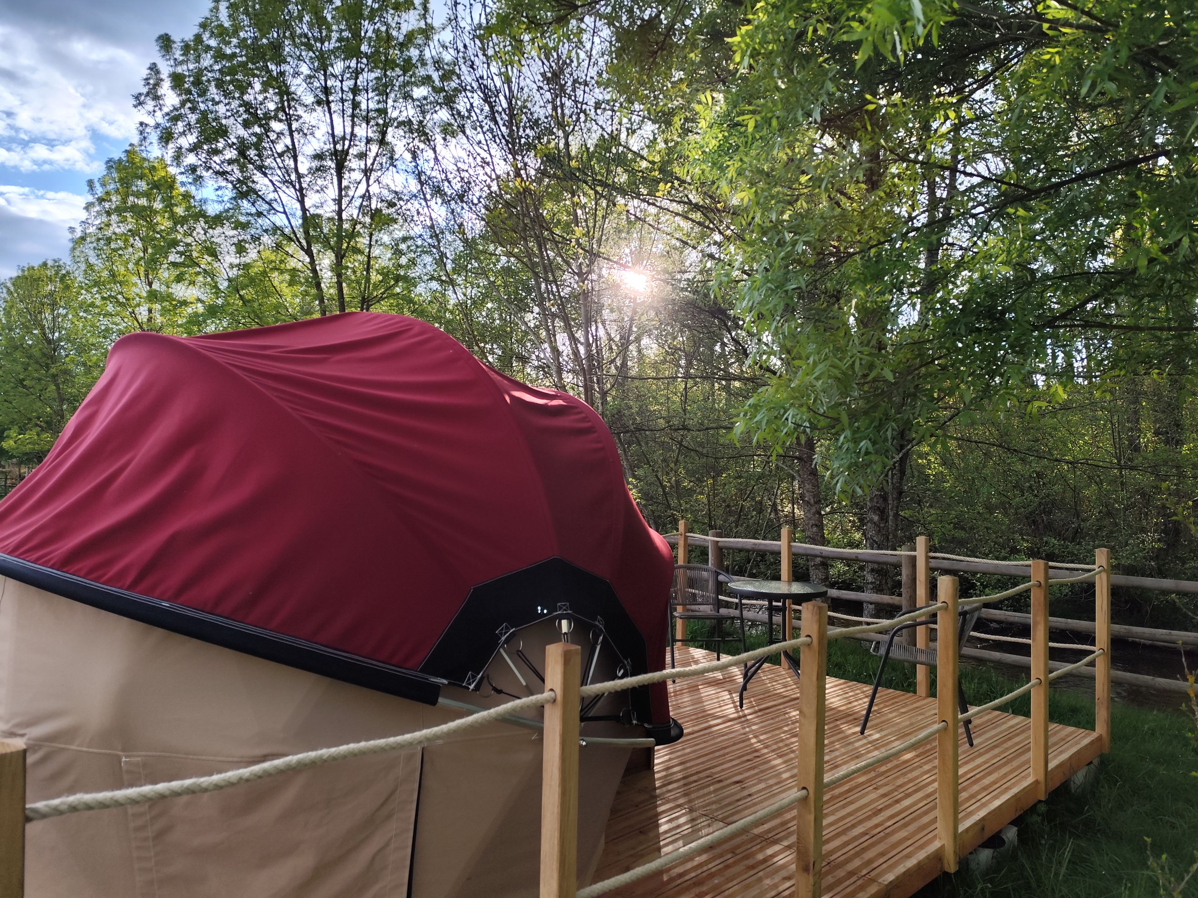 Un véhicule couvert, une terrasse en bois et une barrière faite de cordes, le tout situé dans une zone boisée.