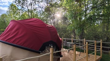 Un véhicule couvert, une terrasse en bois et une barrière faite de cordes, le tout situé dans une zone boisée.